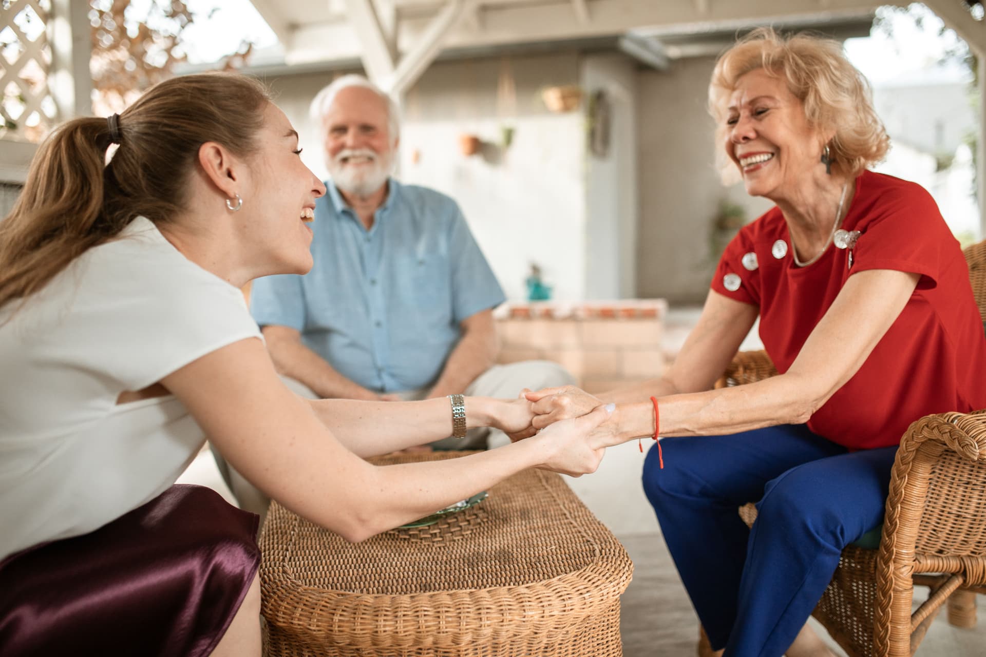 Three adults enjoying a cheerful conversation on a covered patio.